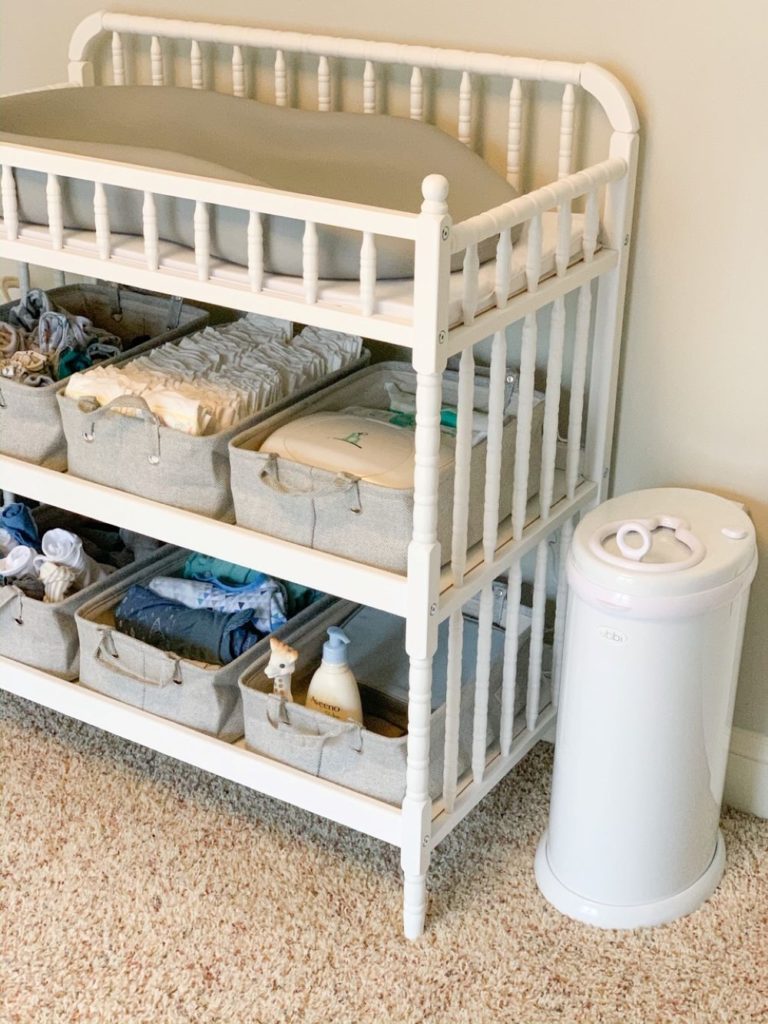 White jenny lind changing table with white and grey storage bins with handles to store changing table essentials, and white diaper pail.