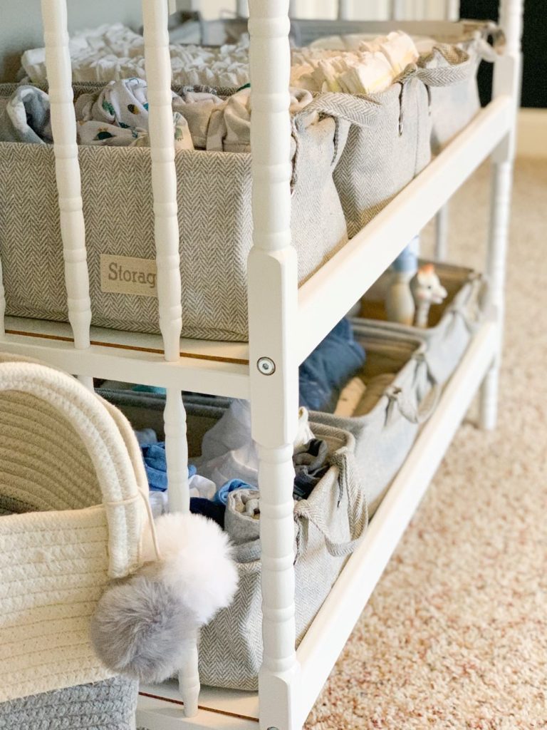 White jenny lind changing table with white and grey storage bins with handles to store changing table essentials.