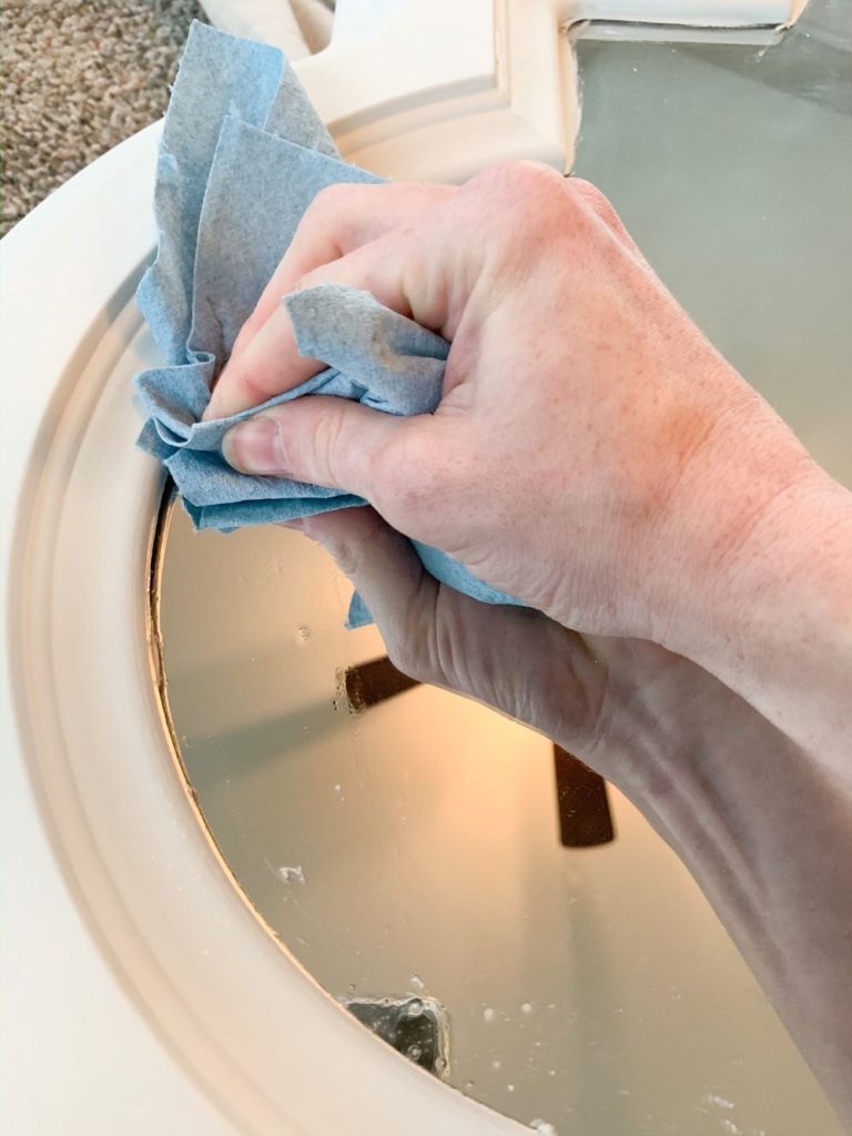 Using a lint free rag with glass cleaner on it to remove the excess paint removed from the scraper and to clean the mirror