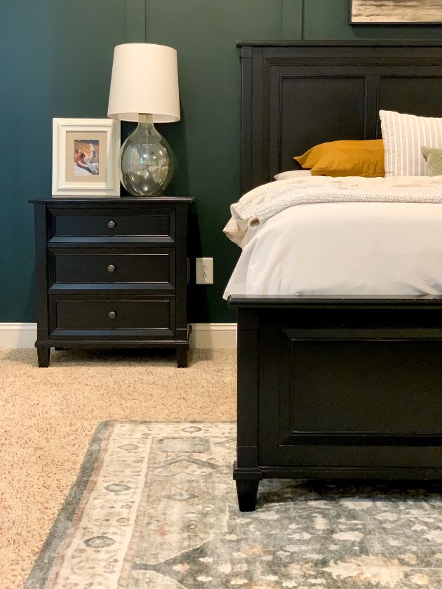 Closeup of black bedroom night stand with bedside lamp and photo. Relaxing master bedroom rug and green focal wall