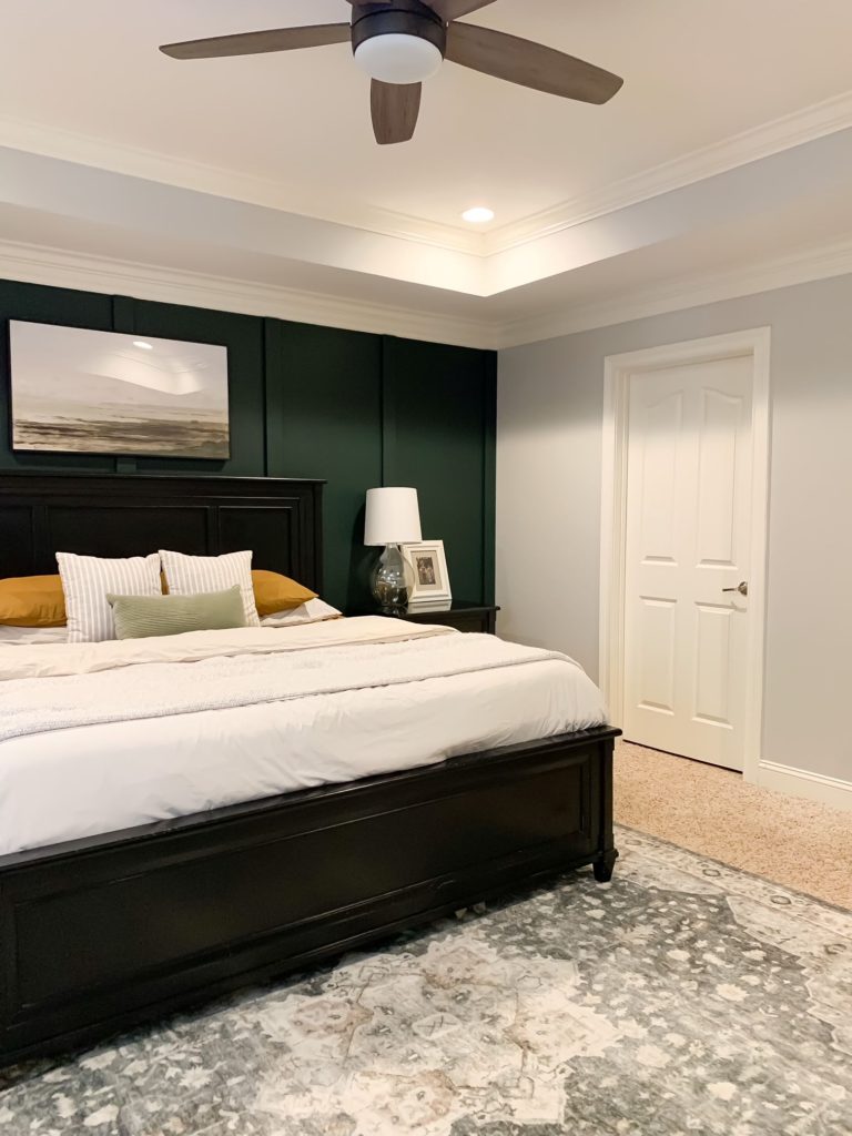 Another angle of full reveal of relaxing master bedroom with green focal wall, landscape art, cream parachute duvet cover, glass bedside lamps, white curtains, and vintage style rug.