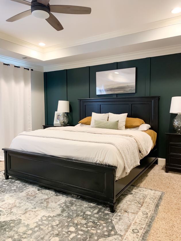 Full reveal of relaxing master bedroom with green focal wall, landscape art, cream parachute duvet cover, glass bedside lamps, white curtains, and vintage style rug.