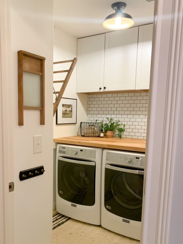 After modern farmhouse laundry room refresh with white cabinetry, white peel and stick subway tile with black grout, and natural butcher block