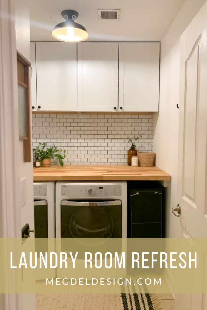 After modern farmhouse laundry room refresh with white cabinetry, white peel and stick subway tile with black grout, and natural butcher block. Jute rug, dark olive green laundry basket.
